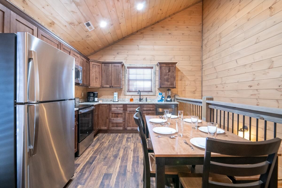Una cocina compacta con paredes de madera, un refrigerador de acero inoxidable, un microondas y una mesa de comedor preparada para cuatro.