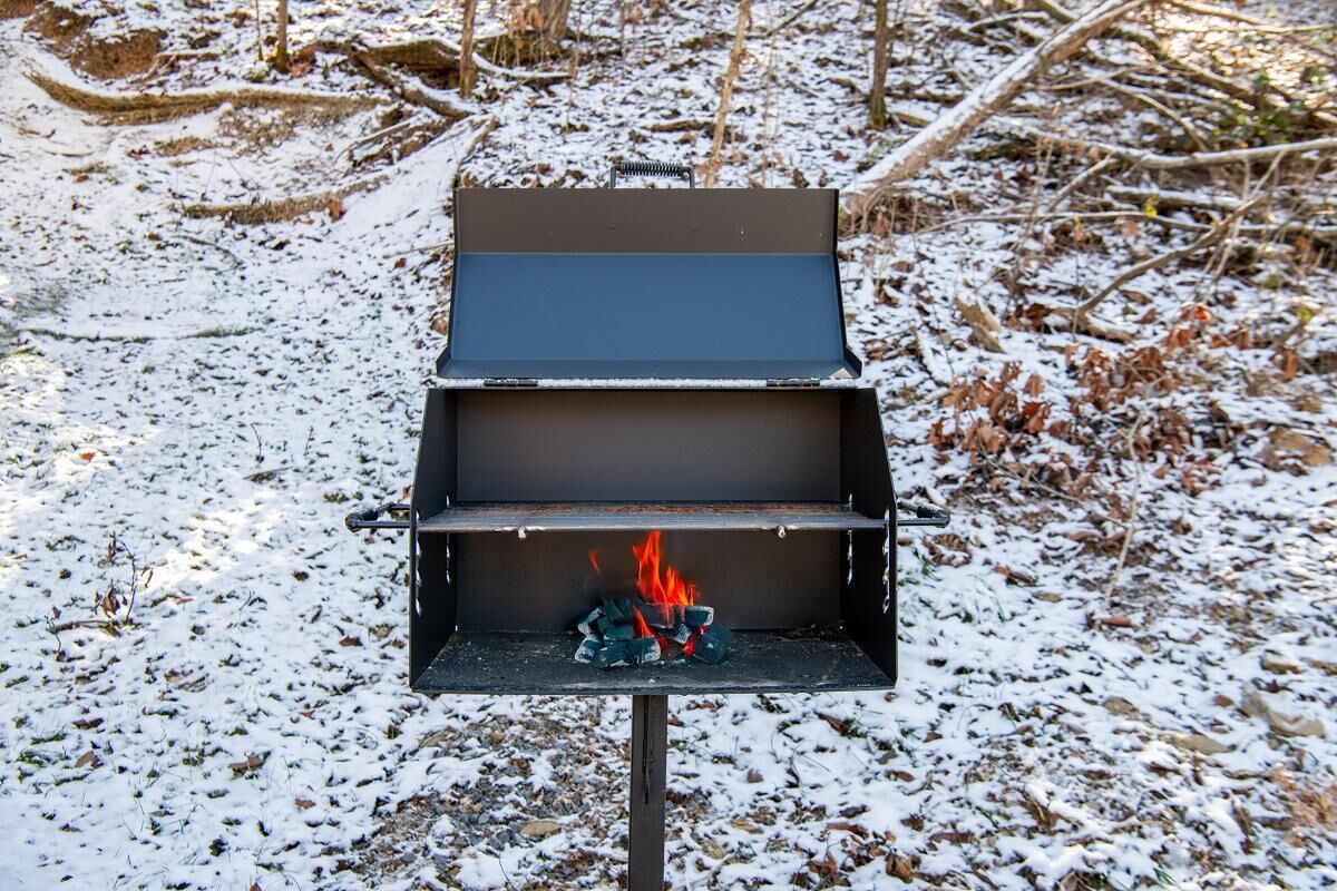 A portable grill with a fire burning inside, set on a snowy ground.