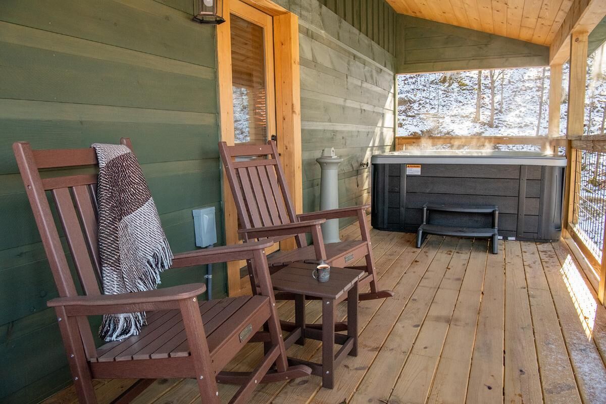 A wooden deck with two rocking chairs, a fireplace, and a hot tub.