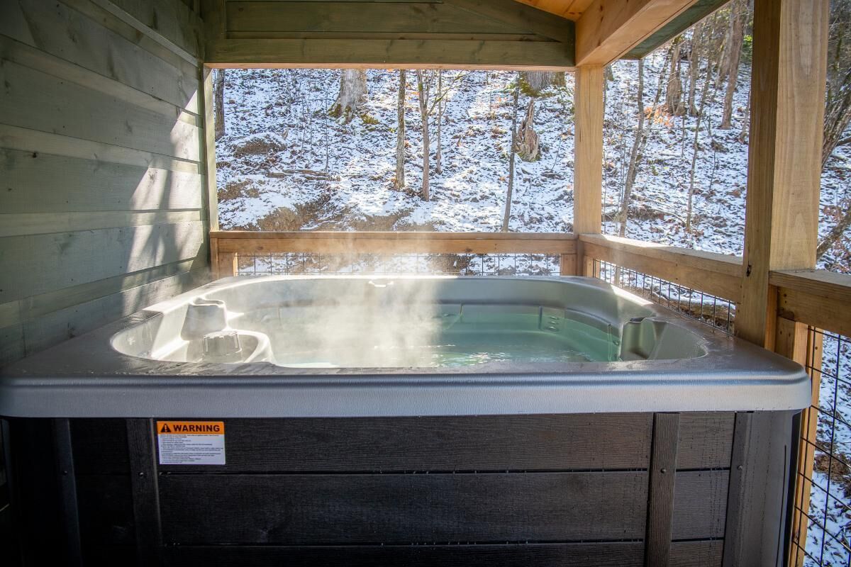 Un jacuzzi en una cabaña de madera con vista a un bosque nevado.