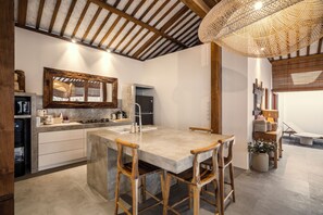 A modern kitchen with a large island, wooden chairs, and a hanging light fixture. - Villa Surya Tanah by Alfred in Bali (Seminyak)