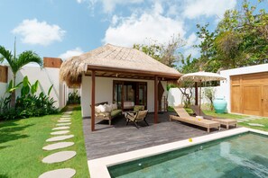 A poolside area with a covered seating area, a wooden deck, and a thatched-roof structure. - Villa Surya Tanah by Alfred in Bali (Seminyak)
