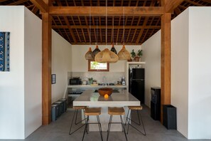 A modern kitchen with a central island, hanging wicker pendant lights, and a black refrigerator. - Villa Surya Tanah by Alfred in Bali (Seminyak)