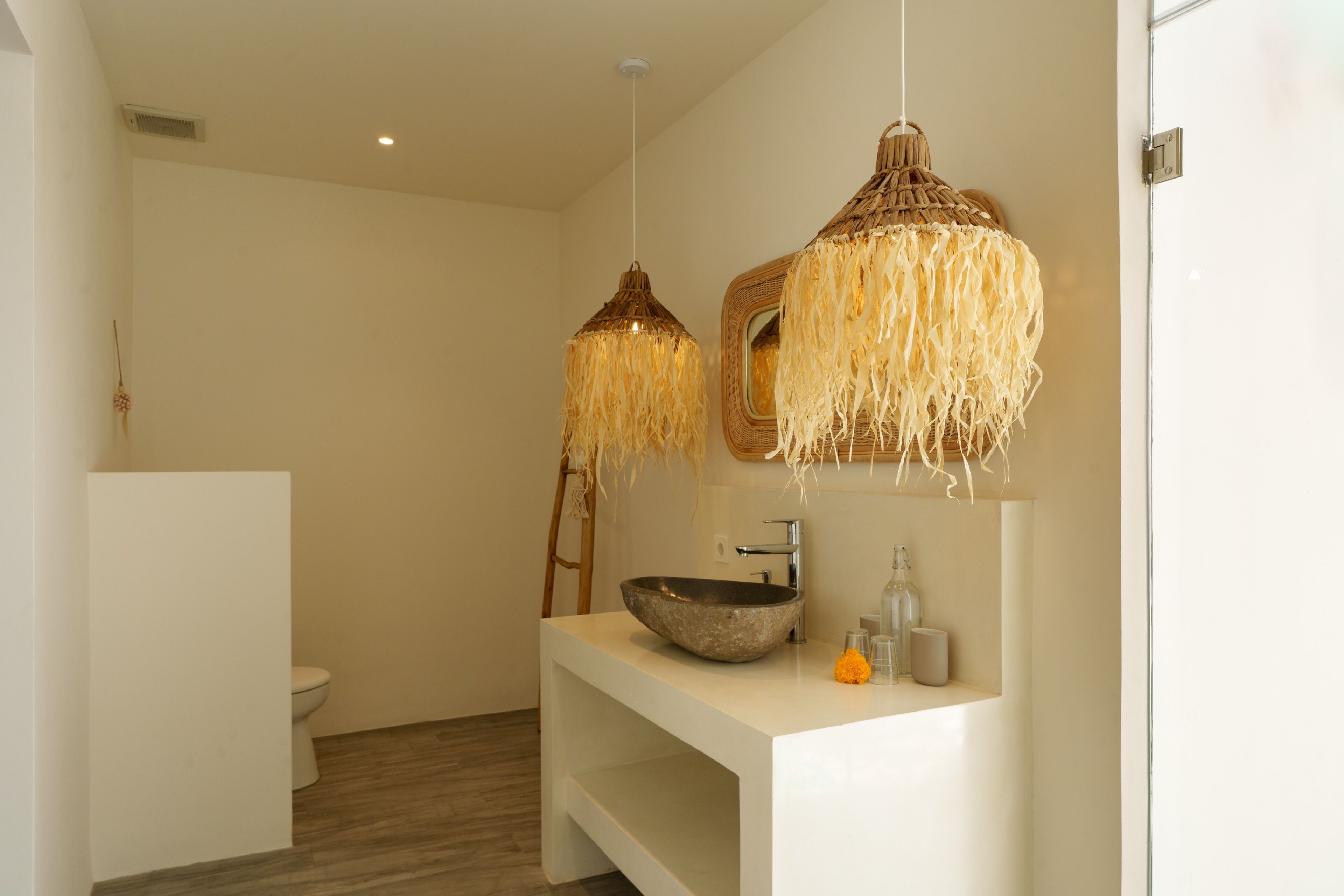 A modern bathroom with a white vanity, a large bowl sink, and two hanging light fixtures with natural fiber strands.