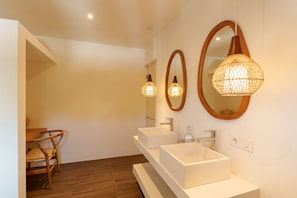 A modern bathroom with two white sinks, a wooden chair, and a large mirror with a woven light fixture. - Villa Surya Tanah by Alfred in Bali (Seminyak)