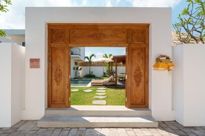 A wooden entrance with a pool and outdoor seating. - Villa Surya Tanah by Alfred in Bali (Seminyak)