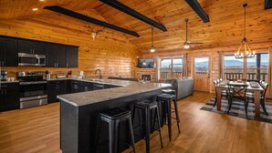 Une cuisine moderne dotée d’un grand îlot central, de tabourets de bar noirs et d’un coin repas offrant une vue agréable.