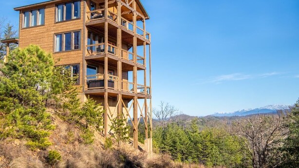 A multi-story wooden building with balconies, surrounded by trees and a mountainous landscape. - Z - Smoky Peaks Pool Cabin (Sevierville)