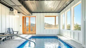 An indoor swimming pool with a view of the outdoors, a wooden door, and a chair by the pool. - Z - Smoky Peaks Pool Cabin (Sevierville)