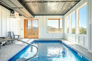 Ein Hallenbad mit Blick ins Freie, eine Holztür und ein Stuhl am Pool.