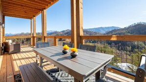 A wooden deck with a table and chairs, overlooking a mountainous landscape. - Z - Smoky Peaks Pool Cabin (Sevierville)