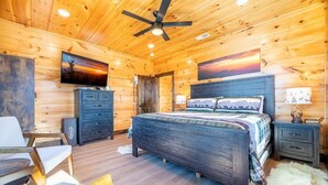 A log cabin bedroom with a bed, a desk, a chair, a television, and a ceiling fan. - Z - Smoky Peaks Pool Cabin (Sevierville)
