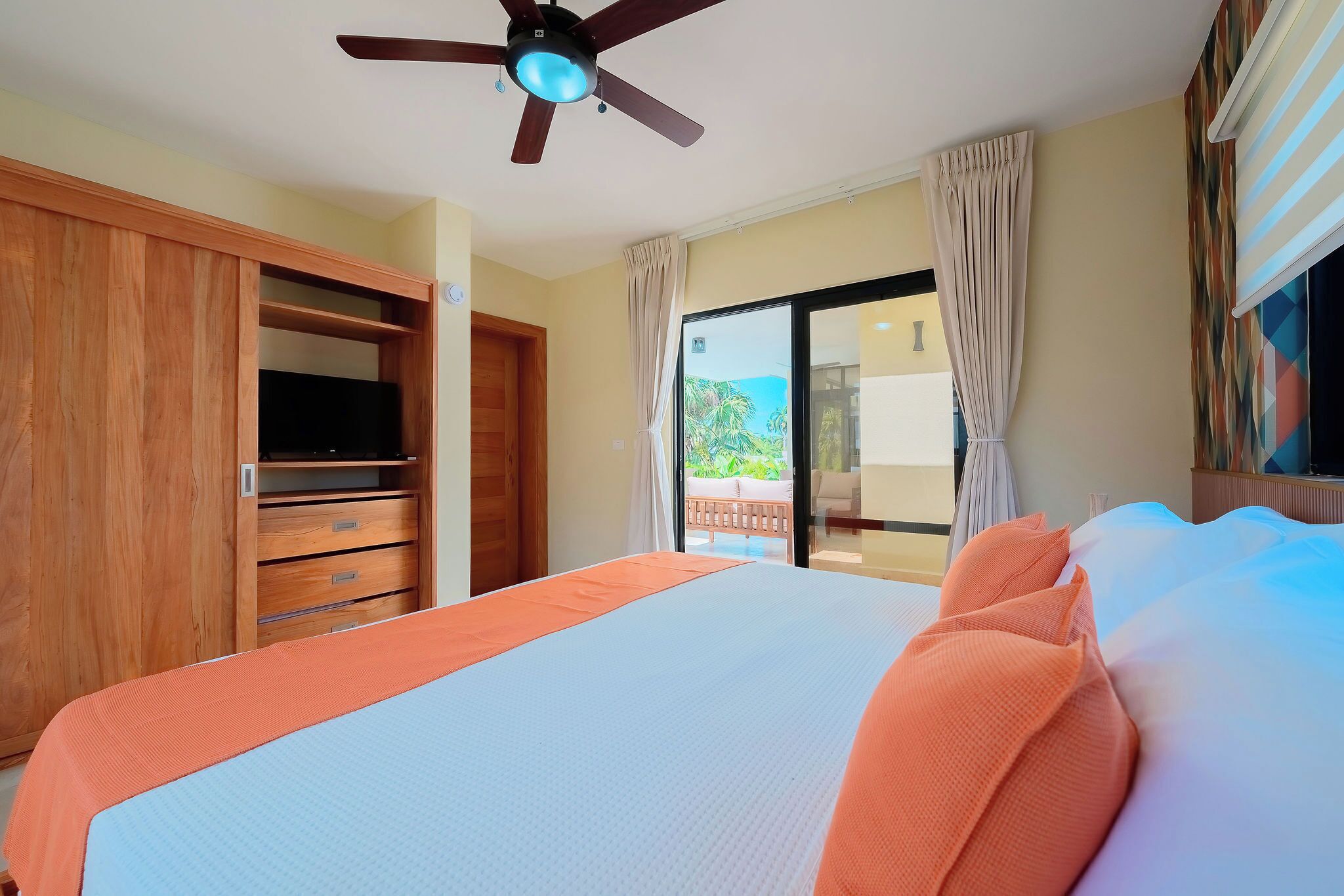 Un dormitorio con cama, armario de madera, ventilador de techo y vistas al exterior a través de una puerta corredera.