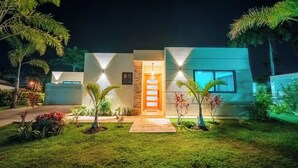 Ein modernes Haus mit einer gut beleuchteten Eingangspartei, einer Steinwand und einem kleinen Garten mit verschiedenen Pflanzen.