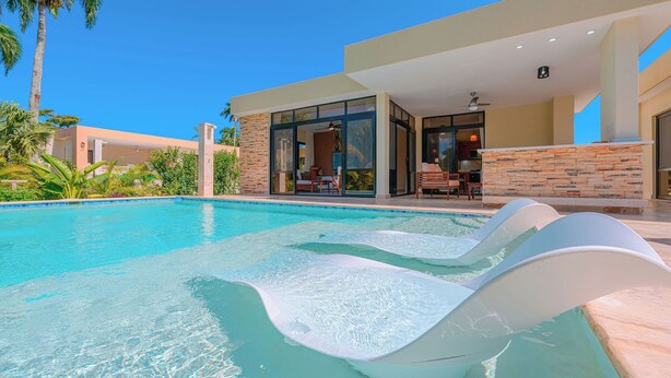 Ein moderner Pool mit klarem Wasser und einer integrierten Rutsche, umgeben von einer begrünten Anlage mit Palmen.