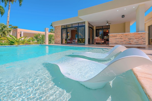 A modern pool with clear water and a built-in slide, surrounded by a landscaped area with palm trees. - Villa Tranquila, Luxury Boho Encuentro Retreat (sosua)
