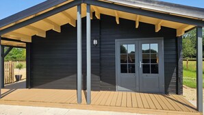 Un espacio al aire libre cubierto con piso de madera, una puerta con paneles de vidrio y un farol.