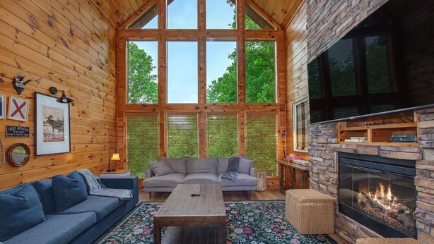 A log cabin interior with a large fireplace, a sofa, a coffee table, and a large window. - Grizzly Grotto (Sevierville)