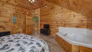 A log cabin room with a bed, a ceiling fan, a TV, and a bathtub. - Grizzly Grotto (Sevierville)