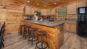A kitchen with wooden paneling, a granite countertop, bar stools, a refrigerator, and a microwave. - Grizzly Grotto (Sevierville)