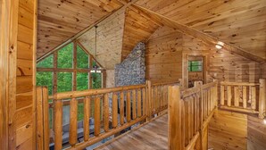 A wooden cabin interior with a stone fireplace, wooden deck, and large windows. - Grizzly Grotto (Sevierville)