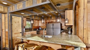 A kitchen with wooden cabinets, a granite countertop, stainless steel appliances, and bar stools. - Summit Castle (Sevierville)