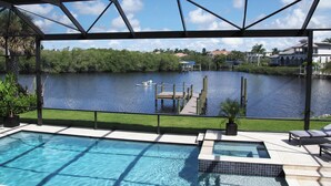 A pool area with a view of a lake, dock, and houses in the background. - Villa Imperial Bonita Springs 5 minutes to the beach, 4 bed/3 bath (Bonita Springs)