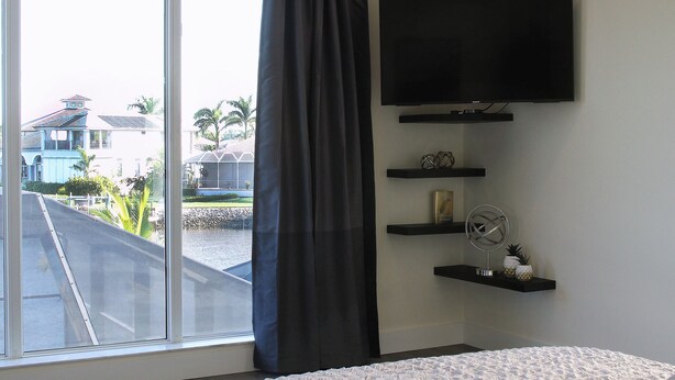 A bedroom with a large bed, a TV mounted on the wall, and a window with a curtain. - Villa Imperial Bonita Springs 5 minutes to the beach, 4 bed/3 bath (Bonita Springs)