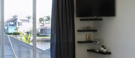A bedroom with a large bed, a TV mounted on the wall, and a window with a curtain.