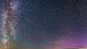 Cel nocturn amb estrelles i la Via Làctia, una calma massa d'aigua i un moll que s'endinsa a l'aigua.
