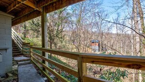 A covered wooden deck with a concrete pathway leading to a staircase. - Bear View Chalet (Gatlinburg)