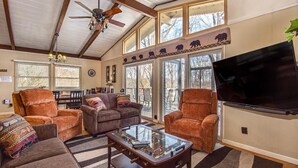 A living room with a sofa, armchairs, a glass coffee table, a ceiling fan, a TV, and large windows. - Bear View Chalet (Gatlinburg)