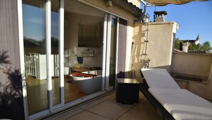 Ein Balkon mit einer Schiebetür zu einem Badezimmer, einem Liegestuhl und einem kleinen Tisch.