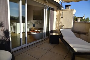 Ein Balkon mit einer Schiebetür zu einem Badezimmer, einem Liegestuhl und einem kleinen Tisch.
