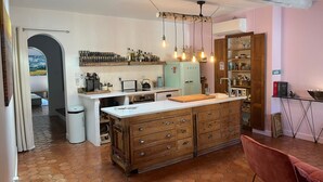 Eine Küche mit einer zentralen Kochinsel, Holzschränken, einem Kühlschrank und einer Pendelleuchte.