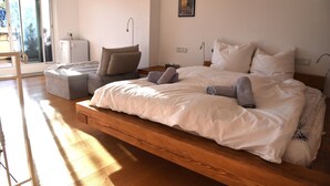 Ein geräumiges Schlafzimmer mit einem großen Bett, einem Nachttisch, einem Sessel und Blick ins Freie.