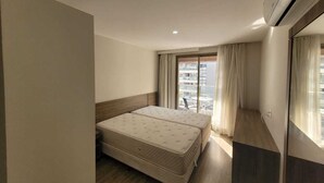 A hotel room with a bed, a window with curtains, and an air conditioning unit. - Suite with garage - Camorim (Rio de Janeiro)