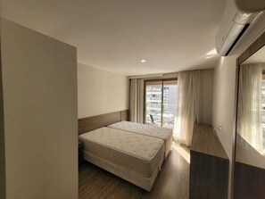 A hotel room with a bed, a window with curtains, and an air conditioning unit. - Suite with garage - Camorim (Rio de Janeiro)