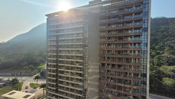 A high-rise building with multiple balconies, surrounded by greenery and a mountain in the background. - Suite with garage - Camorim (Rio de Janeiro)