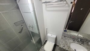 A bathroom with a glass shower enclosure, a toilet, a sink with a granite countertop, and a towel rack. - Suite with garage - Camorim (Rio de Janeiro)