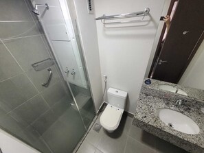 A bathroom with a glass shower enclosure, a toilet, a sink with a granite countertop, and a towel rack. - Suite with garage - Camorim (Rio de Janeiro)