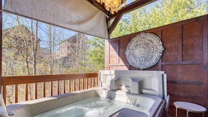 Een hottub met een houten terras, een decoratieve wandplaat en een kleine tafel.