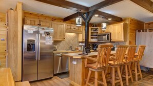 A kitchen with wooden cabinets, a stainless steel refrigerator, a microwave, and a wooden island with bar stools. - Honey Bear Lodge (Gatlinburg)