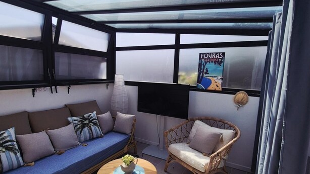 A sunlit room with a sofa, a chair, a small table with a plant, and a wall-mounted TV. - A seaside getaway for two in the heart of Fouras (FOURAS)