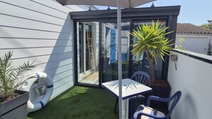 A small patio with artificial grass, a table, chairs, a potted plant, and a sliding glass door leading to an adjacent room. - A seaside getaway for two in the heart of Fouras (FOURAS)