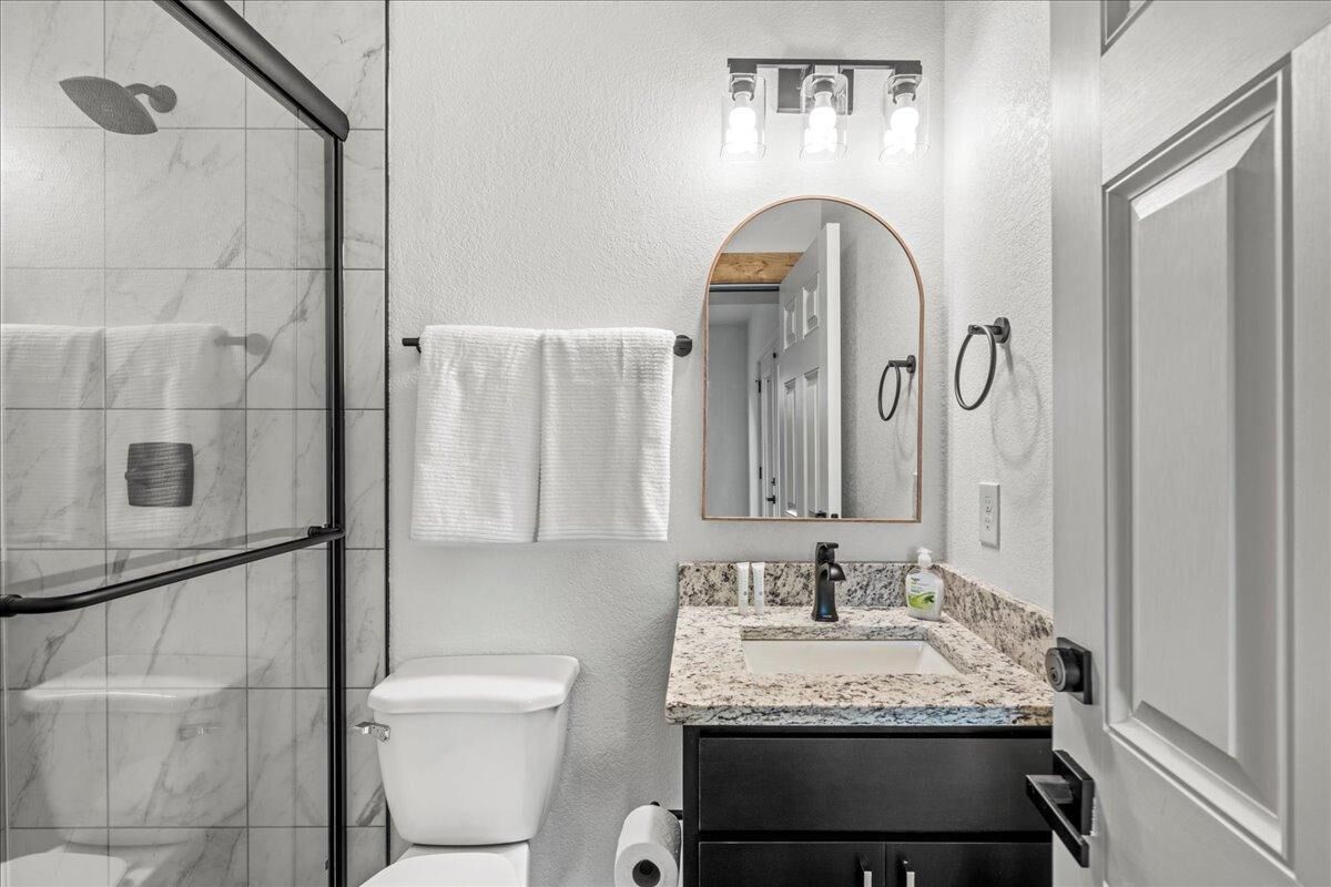 Une salle de bain moderne dotée d’une douche à parois de verre, de toilettes, d’un lavabo avec un plan de travail en marbre et d’un miroir surmonté d’un arc.