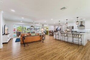 Una cocina amplia con suelo de madera, armarios blancos e iluminación colgante.