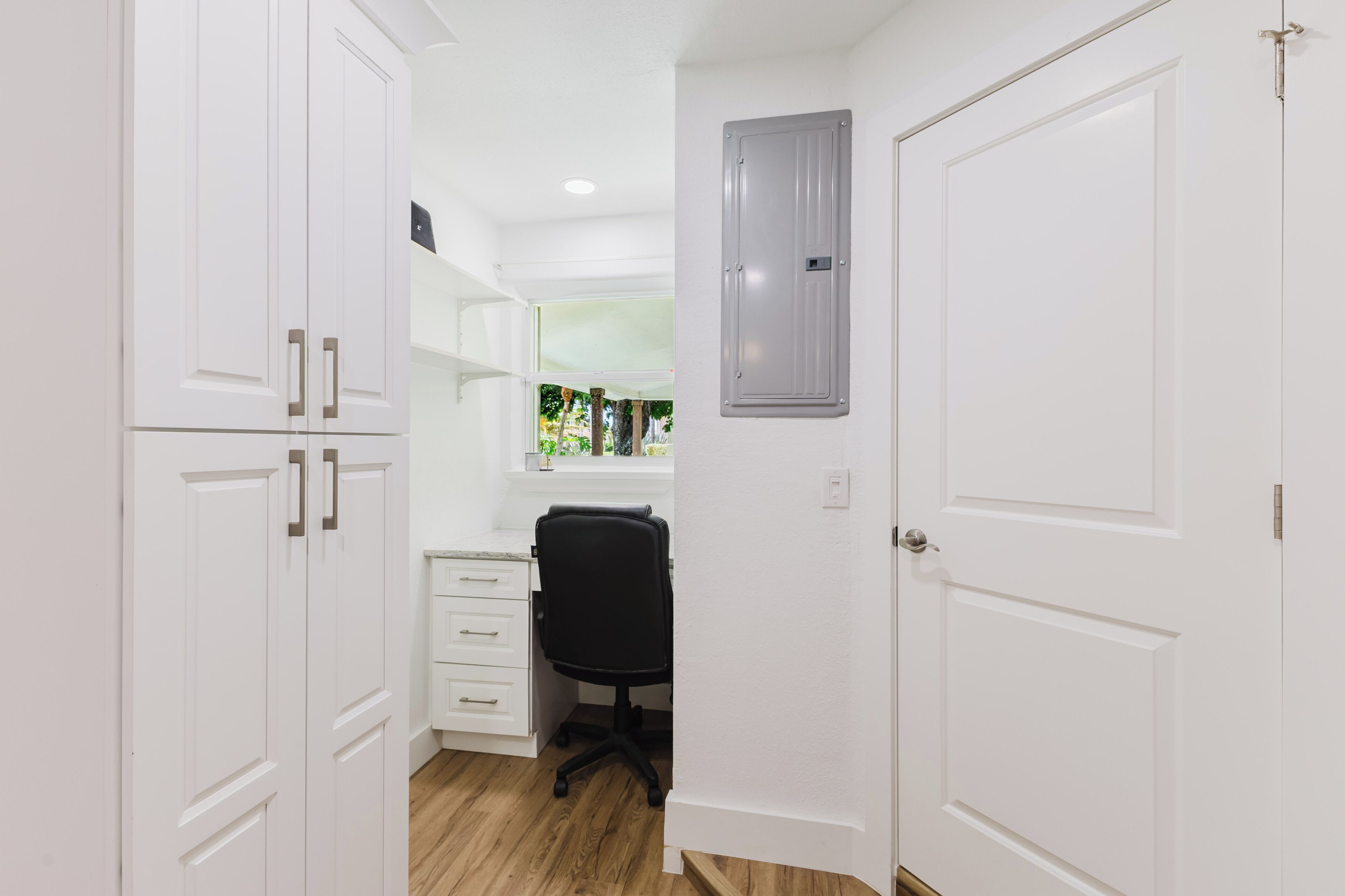 A narrow hallway with white doors, a black office chair, and a window with a view of greenery.
