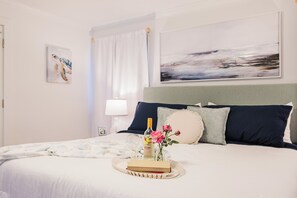 Een net opgemaakt bed met een dienblad, een schilderij aan de muur en een raam met gordijnen.