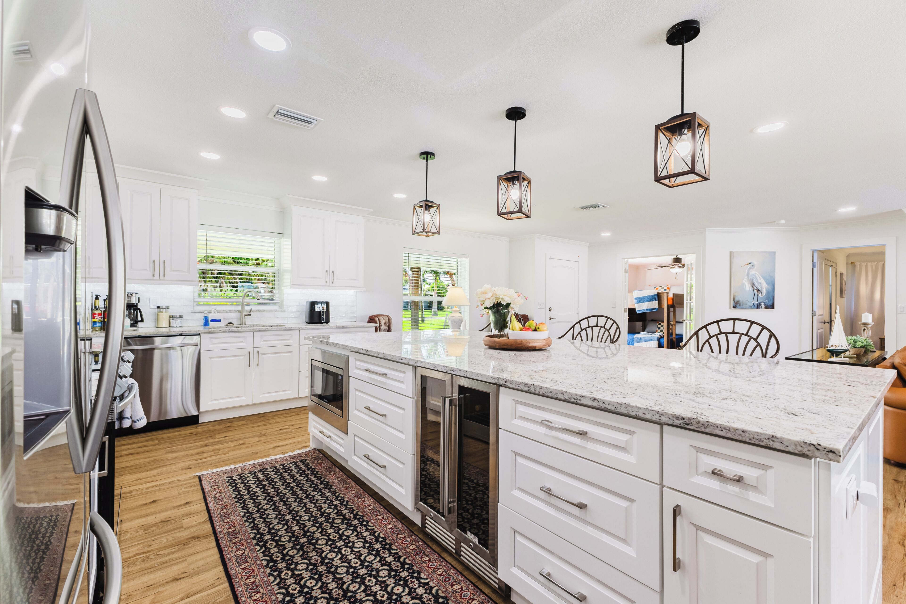 Une cuisine moderne avec des meubles blancs, un grand îlot central, des appareils en acier inoxydable et des luminaires suspendus.